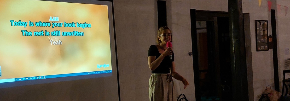 Frau singt Karaoke, im Hintergrund eine Leinwand mit Liedtext.