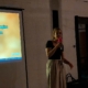 Frau singt Karaoke, im Hintergrund eine Leinwand mit Liedtext.